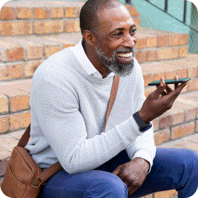 A senior man holds his phone in front of his face while talking on speaker phone. 